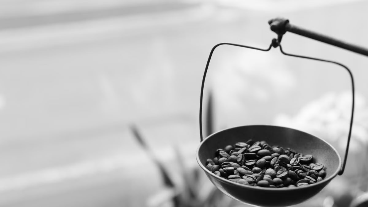 Artistic black and white photo of coffee beans on a balance scale, evoking a rustic yet modern feel.